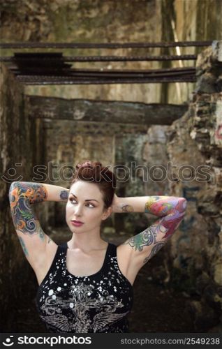 Sexy tattooed Caucasian woman standing next to concrete wall.