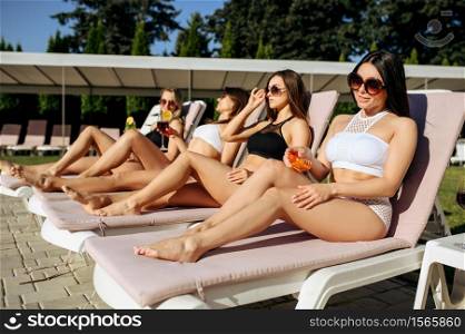 Sexy woman applies tanning spray on sunbed, sunbathing. Beautiful girls relax at the poolside in sunny day, summer vacation of attractive girlfriends. Sexy woman applies tanning spray on sunbed