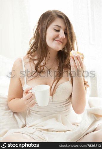 Sexy woman having breakfast in bed with coffee and donut