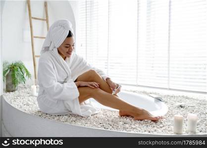 Sexy woman in bathrobe sitting on the edge of the tub. Female person in bathtub, beauty and health care in spa, wellness treathment in bathroom, pebbles and candles on background. Sexy woman in bathrobe sitting on the edge of tub