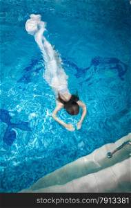 Sexy woman in long white dress diving underwater at swimming pool