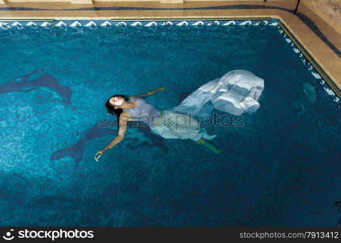 Sexy woman in long white dress swimming on water surface at swimming pool