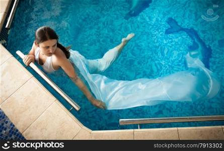 Sexy woman in white dress swimming next to edge in swimming pool