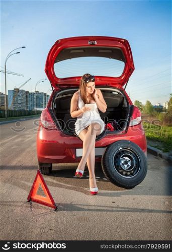 Sexy woman leaning against broken car and browsing hot to repair it on tablet