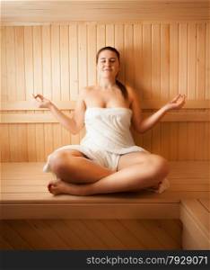 Sexy woman meditating on bench at sauna