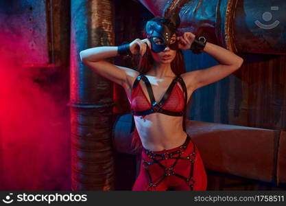 Sexy woman poses in bdsm suit and leather mask, abandoned factory interior on background. Young girl in erotic underwear, sex fetish, sexual fantasy. Sexy woman poses in bdsm suit and leather mask