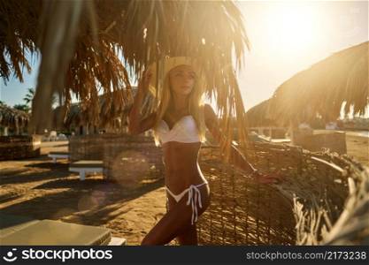 Sexy woman wearing bikini standing under straw canopy umbrella at the beach.. Sexy woman wearing bikini standing under straw canopy umbrella at the beach