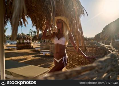 Sexy woman wearing bikini standing under straw canopy umbrella at the beach.. Sexy woman wearing bikini standing under straw canopy umbrella at the beach