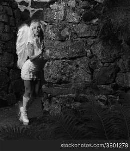 Sexy woman wearing white angel costume and wings, she leans to the stone wall - motion blurring, combination of natural and flash lights