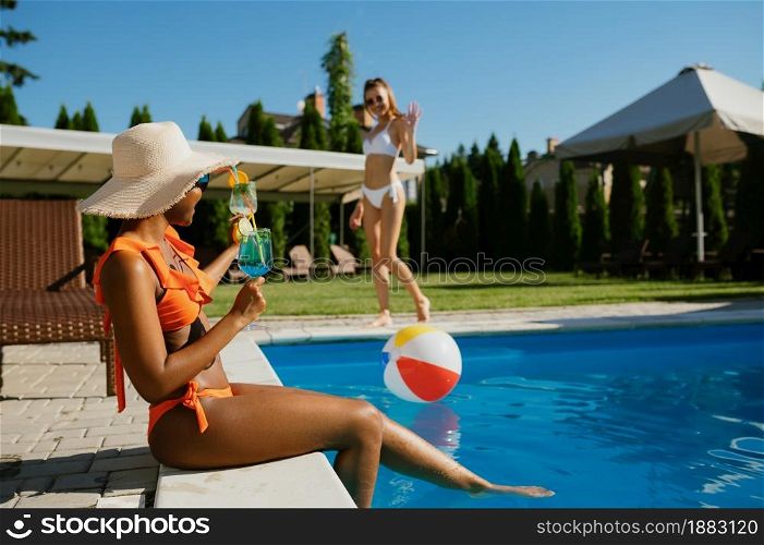 Sexy woman with coctail sitting at the edge of the pool. Happy people having fun on summer vacations, holiday party at the poolside outdoors. Female person leisures at the resort. Woman with coctail sitting at the edge of the pool