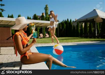 Sexy woman with coctail sitting at the edge of the pool. Happy people having fun on summer vacations, holiday party at the poolside outdoors. Female person leisures at the resort. Woman with coctail sitting at the edge of the pool