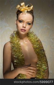 sexy woman with freckles posing in creative christmas portrait with glossy golden make-up, tinsel on nude breast and ribbon in hair-style