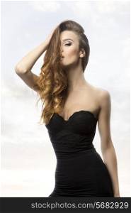 sexy woman with long wavy flowing hair on the face, sexy black dress and cute make-up, in sensual pose in fashion shoot