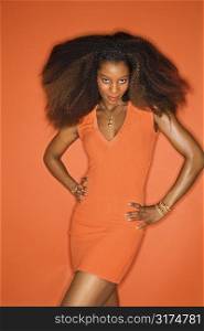 Sexy young African-American adult woman with big hair on orange background wearing dress and looking seductively at viewer.