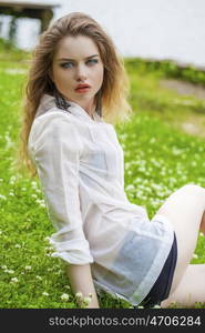 Sexy young blonde woman in white dress sitting on green grass in summer park