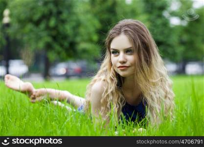 Sexy young blonde woman in white dress sitting on green grass in summer park