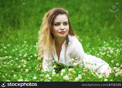 Sexy young blonde woman in white dress sitting on green grass in summer park