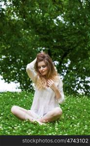 Sexy young blonde woman in white dress sitting on green grass in summer park
