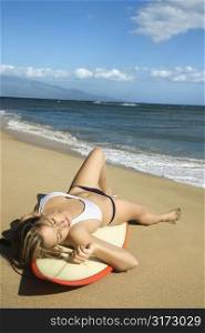 Sexy young Caucasian woman in bikini lying on surfboard sunbathing at beach in Maui Hawaii.
