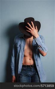 Sexy young cowboy by a blue wall is standing with his shirt open