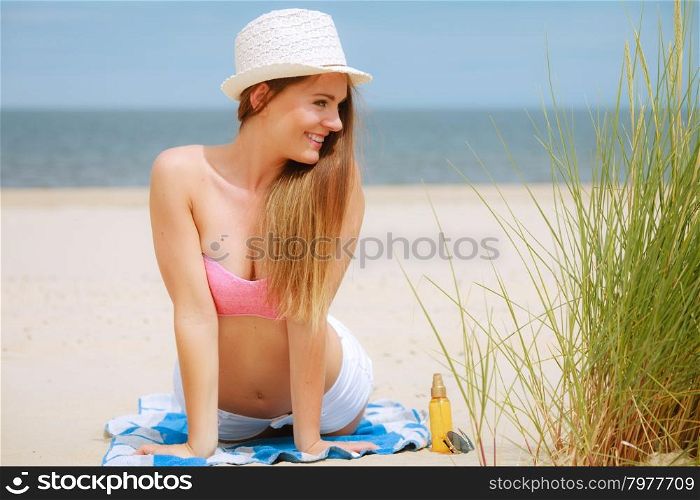 Sexy young girl on beach. Sun protection concept. Attractive sexy long haired woman in straw hat lying on beach with sunscreen body lotion and sunglasses.
