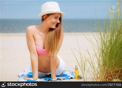 Sexy young girl on beach. Sun protection concept. Attractive sexy long haired woman in straw hat lying on beach with sunscreen body lotion and sunglasses.