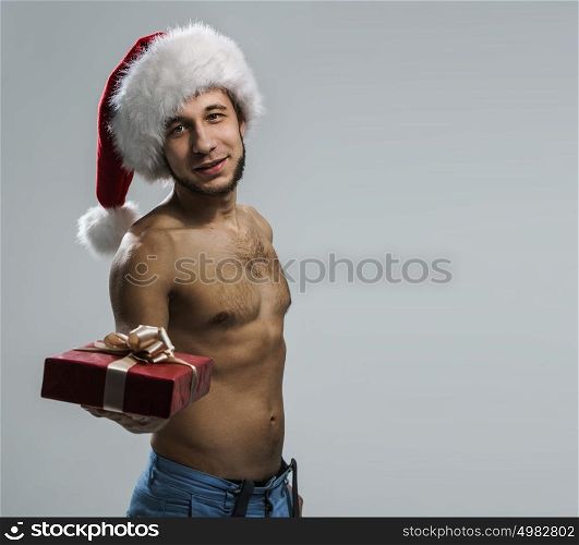 Sexy young man wearing Santa Claus hat holding Christmas gift portrait