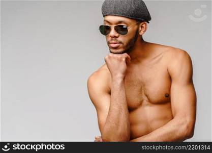 Sexy young muscular african american man shirtless wearing sunglasses and cap over light grey background.. Sexy young muscular african american man shirtless wearing sunglasses and cap over light grey background