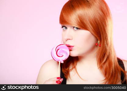 Sexy young woman holding candy. Redhair girl eating sweet lollipop on pink. Studio shot. Sweets.