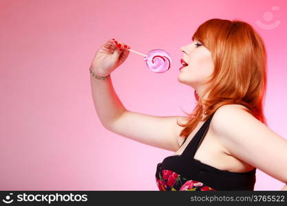 Sexy young woman holding candy. Redhair girl eating sweet lollipop on pink. Studio shot. Sweets.