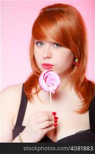 Sexy young woman holding candy. Redhair girl eating sweet lollipop on pink. Studio shot. Sweets.