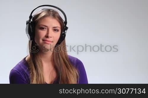 Sexy young woman listening to music playfully puckering up her lips and blowing kiss at the camera on white. Expressive girl with headset enjoying favorite song on the radio and flirting with the cam.