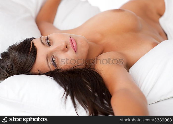 Sexy young woman lying naked in white bed, shallow DOF