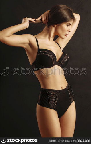 Sexy young woman posing in black underwear over a dark background.