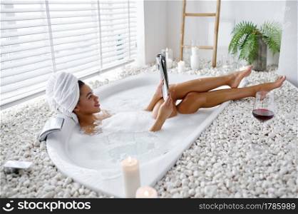Sexy young woman reads a magazine in a bubble bath. Female person in bathtub, beauty and health care in spa, wellness treathment in bathroom, pebbles and candles on background. Sexy young woman reads a magazine in a bubble bath