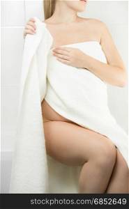 Sexy young woman sitting on side of bath and covering in towel