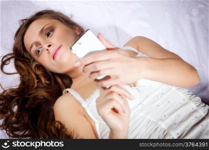 Sexy young woman texting while lying on a bed at home