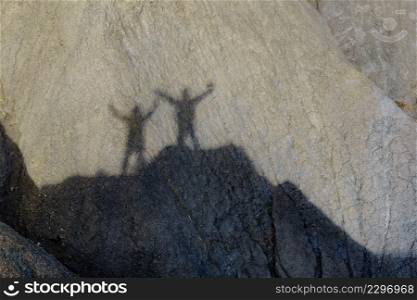 Shadow of two people on rock during hiking in stone mountains. Couple holdings hands, arms raised. Happiness and freedom.. Shadow of two people on rock mountain