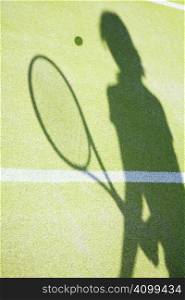 shadow on tennis court of woman hitting the ball