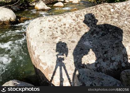 Shadow, silhouette of man with camera on bank of mountain river