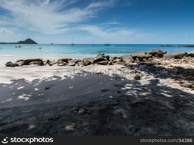 Shadows and rocks on the beach with the sea and boats in the background in Saint Lucia
