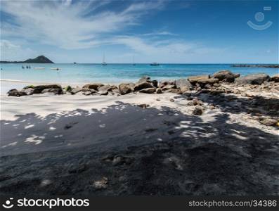 Shadows and rocks on the beach with the sea and boats in the background in Saint Lucia