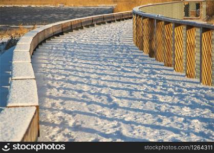 Shadows from railings falling on wooden boardwalk to the mole of Parnu covered by fresh snow in winter morning.