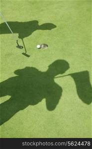 Shadows of two golfers hitting the ball on the golf course, ball in the hole