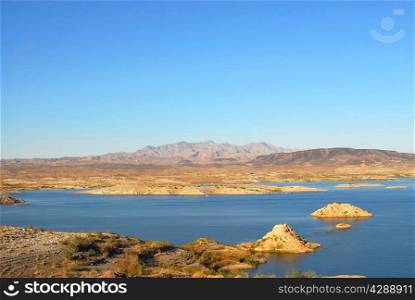 Shallow blue lake and rock outcrops against desert mountain horizon at Lake Mead.