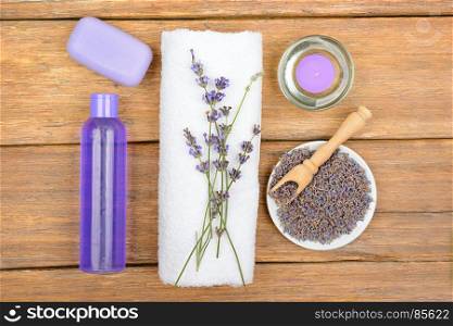 Shampoo, shower gel, liquid soap, aromatic candle made from lavender flowers on a wooden surface