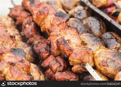 Shashlik and unpeeled whole potatoes on skewers over barbecue