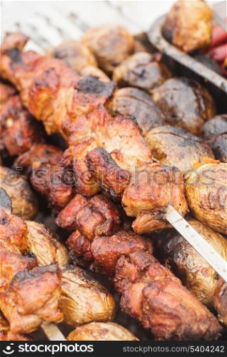 Shashlik and unpeeled whole potatoes on skewers over barbecue