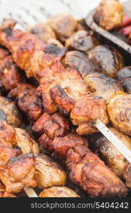 Shashlik and unpeeled whole potatoes on skewers over barbecue