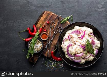 Shashlik marinated for grill in onion, chili peppers and spices. Raw pork meat for spicy shish kebab on skewers on black background, top view